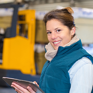 Happy woman carrying out a forklift inspection on a tbalet in a warehouse