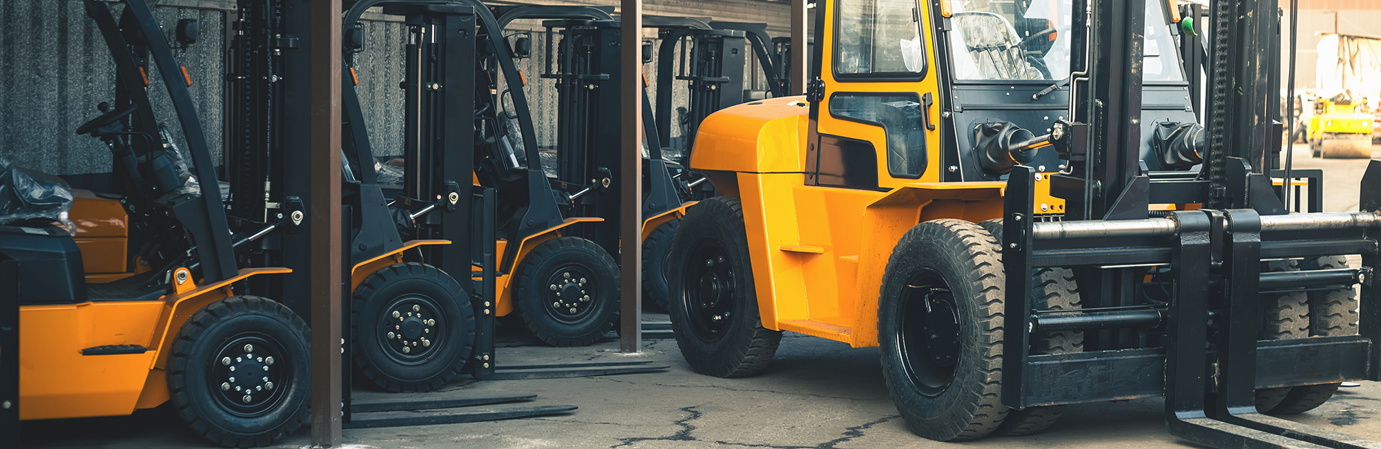 Yellow forklift trucks lined up in a yard with heavy handler in front
