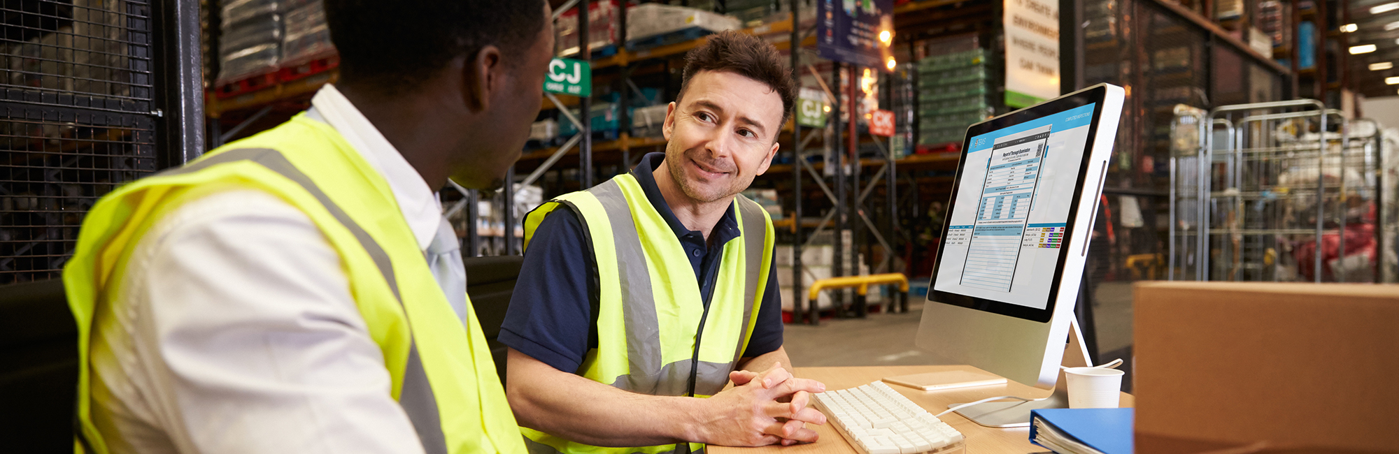 Two men looking sat at warehouse desk looking at report