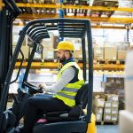 Man driving electric forklift from a side view profile