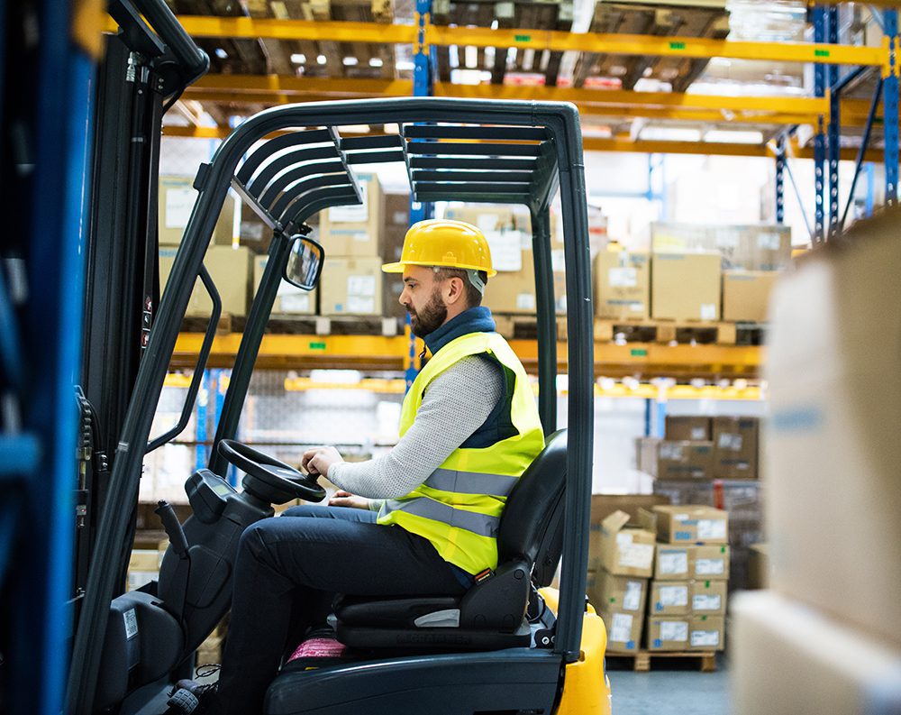 Man driving electric forklift from a side view profile